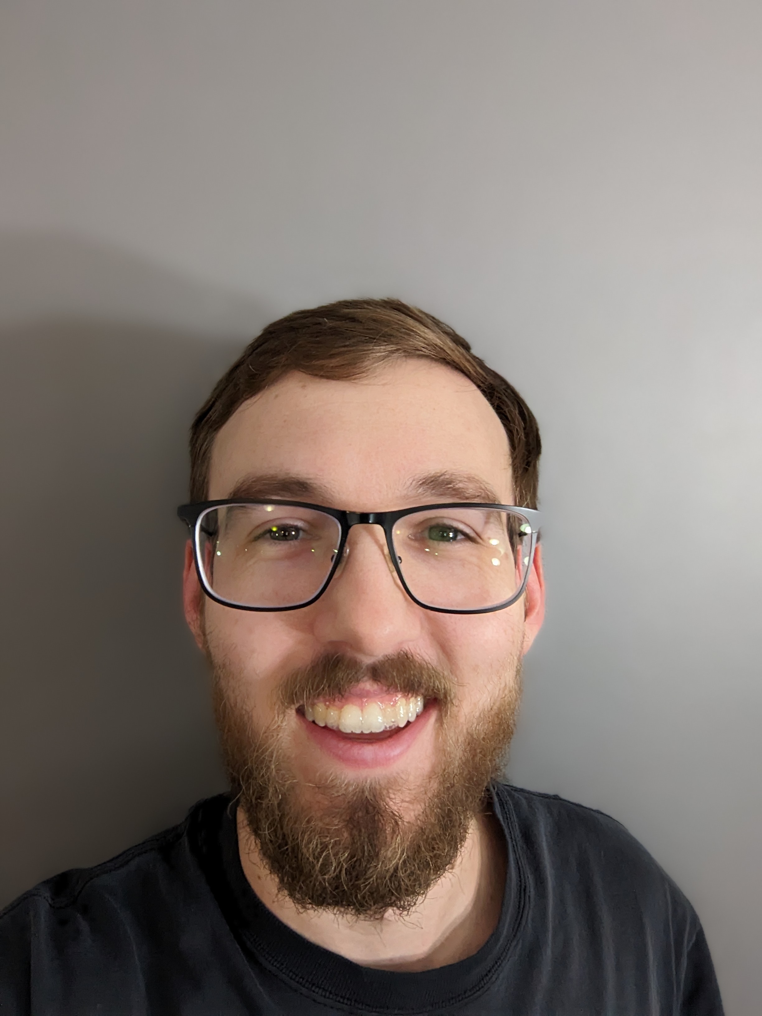 A person wearing glasses with a beard smiles into the camera.