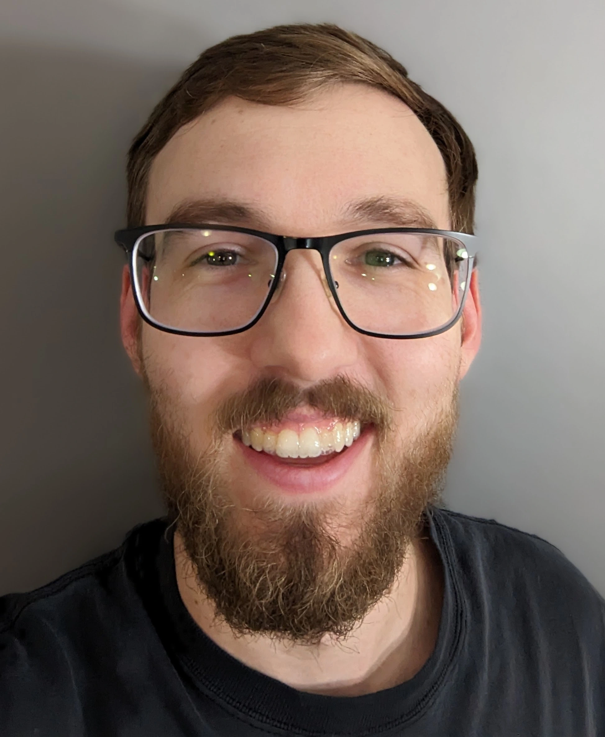 A person wearing glasses with a beard smiles into the camera.